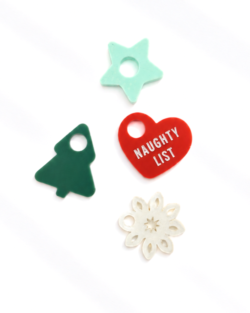 Four Christmas-themed felt charms on a white background: a mint green five-pointed star, a dark green Christmas tree, a red heart with 'NAUGHTY LIST' in white text, and an off-white snowflake.