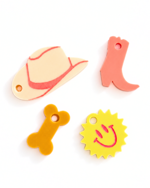 Four small flat foam accessories on a white background: a tan cowboy hat with pink trim, a coral boot, a yellow bone, and a yellow sun with a pink smiley face.